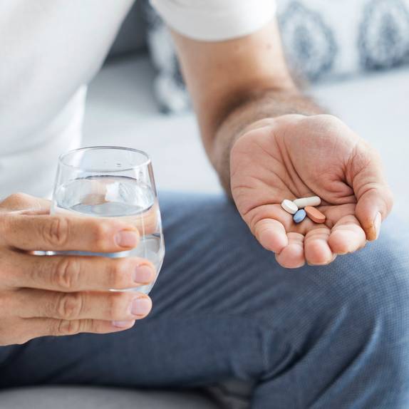 Man holding a glass of water and four pills